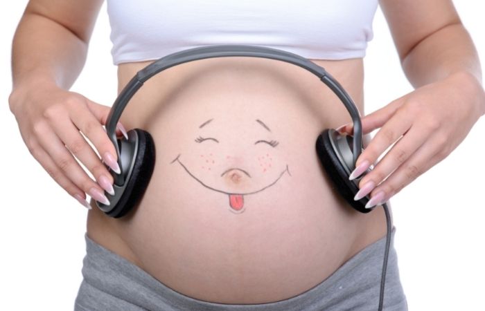 fotos divertidas de embarazo: cara sonriente pintada en la barriga y auriculares