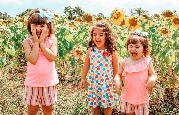 Tres niñas riendo en un campo de girasoles. Coger a un bebé en brazos: beneficios