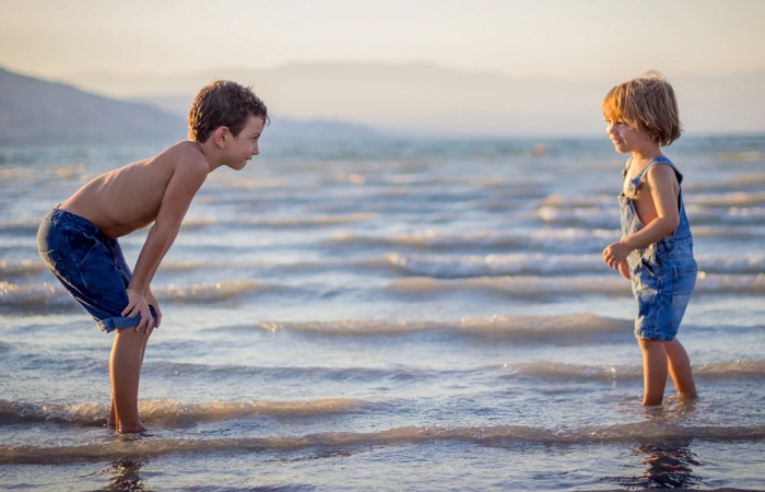Dos niños juegan en la orilla del mar. Coger a un bebé en brazos les da seguridad