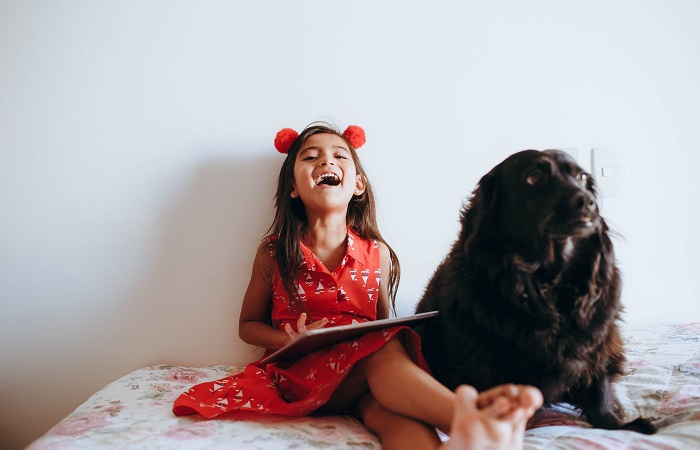 Niña sentada en su cama con el perro a su lado. Alérgico a la mascota síntomas