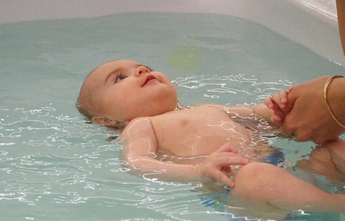 Niño flotando boca arriba en la bañera de un spa con vigilancia adulta Hidroterapia para bebés 