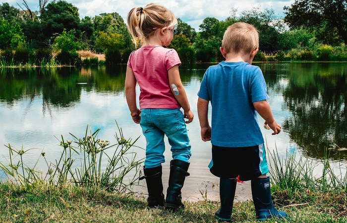 Dos niños pequeños frente a un lago. Jugar con barro beneficia su salud