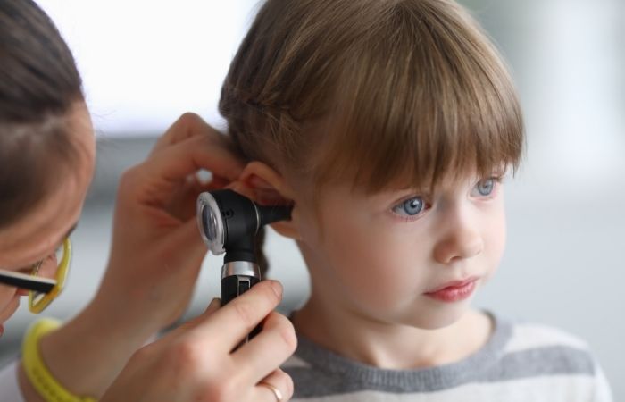 Una doctora inspecciona el oído de una niña con un otoscopio. Otorrea síntomas