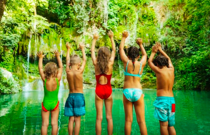 Niños en bañador, de espaldas, miran a un lago. Planes para fin de curso