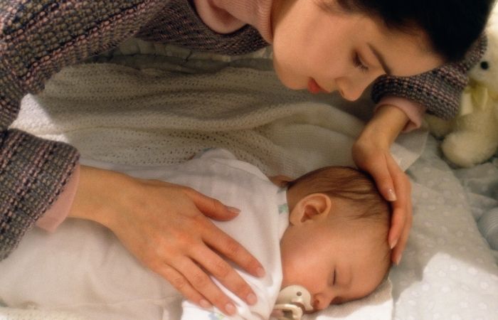 Trastorno Obsesivo Compulsivo postparto: madre tocando con precaución a su bebé dormido en la cuna
